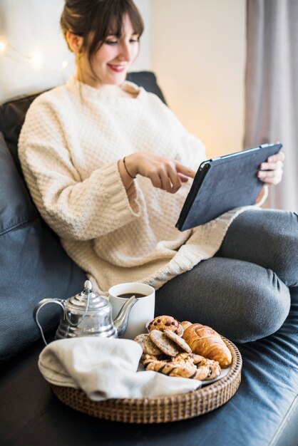 Женщина, используя цифровой планшет с завтраком на диване