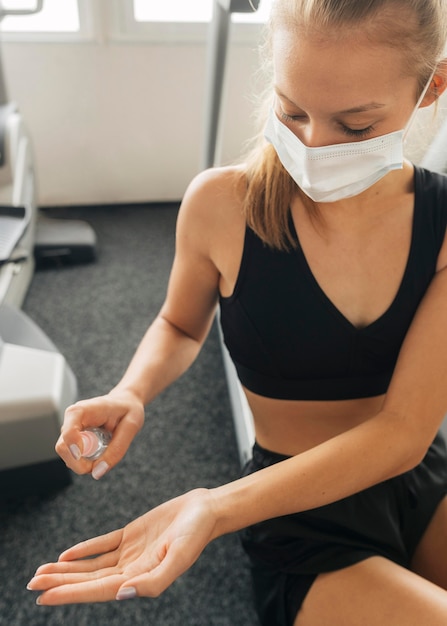 Foto gratuita donna che utilizza un disinfettante per le mani mentre indossa una maschera medica in palestra