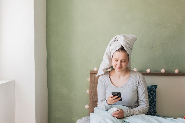 女性がベッドで彼女のスマートフォンを使用して