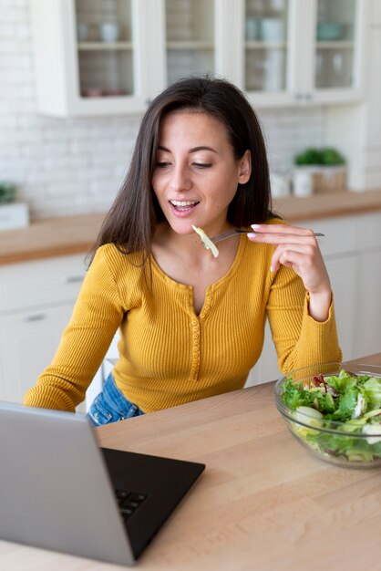Женщина использует ноутбук и ест салат