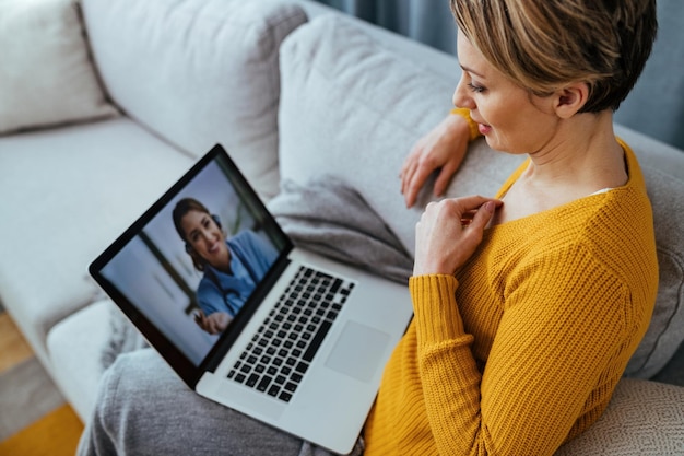 Женщина использует ноутбук и разговаривает по видеосвязи со своим врачом, сидя дома