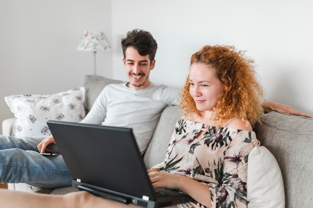 Foto gratuita donna che utilizza computer portatile che si siede vicino a suo marito sul divano