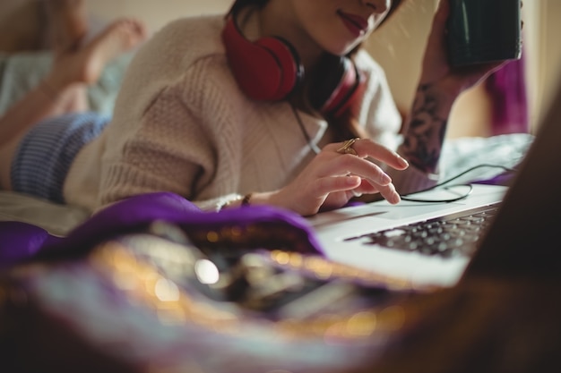 Foto gratuita donna che utilizza computer portatile mentre si prende il caffè sul letto