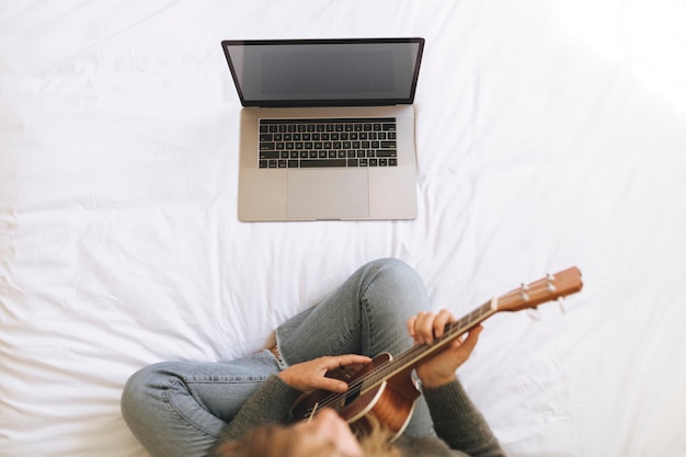 Woman using a laptop while playing ukulele during lockdown