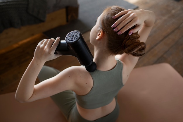 Foto gratuita donna che utilizza la pistola per massaggio ad alto angolo