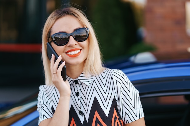 Foto gratuita donna che utilizza il telefono cellulare, la comunicazione o l'applicazione online, in piedi vicino all'auto sulla strada della città o sul parcheggio, all'aperto. car sharing, servizio di noleggio