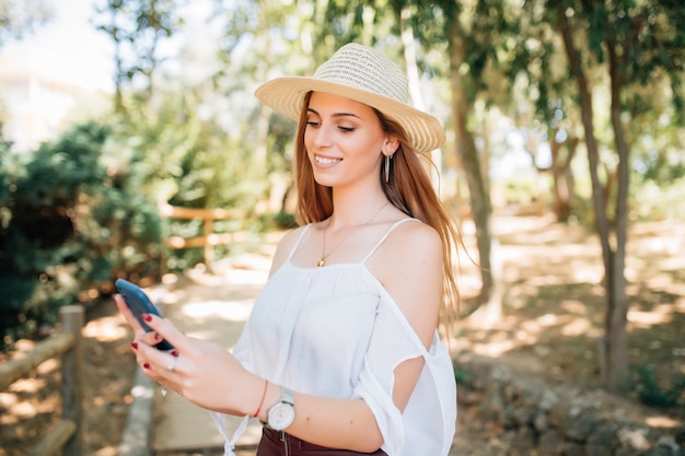 Woman using mobile phone in the park, green trees on background. Communication concept