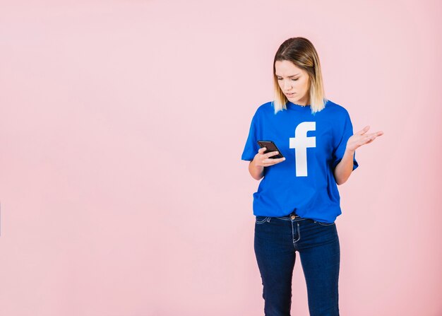 woman using mobile phone shrugging against pink background