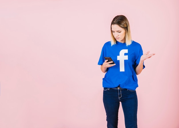 Woman using mobile phone shrugging against pink background