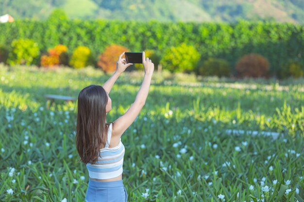 フラワーガーデンで写真を撮るために携帯電話を使用している女性。