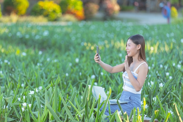 여자는 꽃밭에서 사진을 찍기 위해 휴대 전화를 사용합니다.