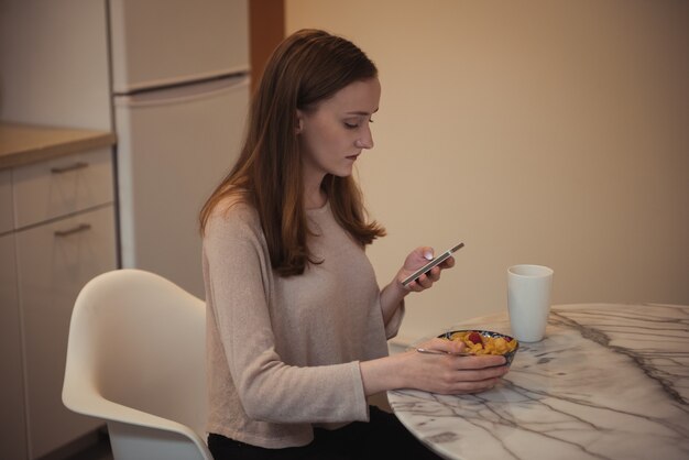 キッチンで朝食をとりながら携帯電話を使用している女性
