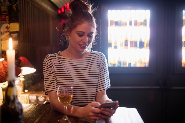 Woman using mobile phone with wine on table