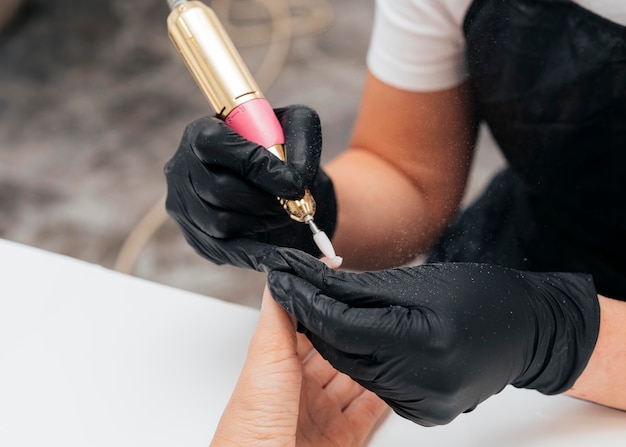 Woman using a nail file on client and wearing gloves