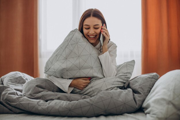 朝ベッドで電話を使用している女性