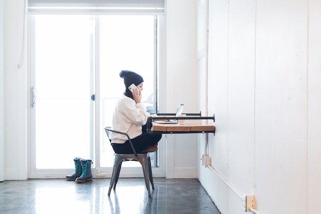 Женщина, используя телефон и ноутбук в офисе