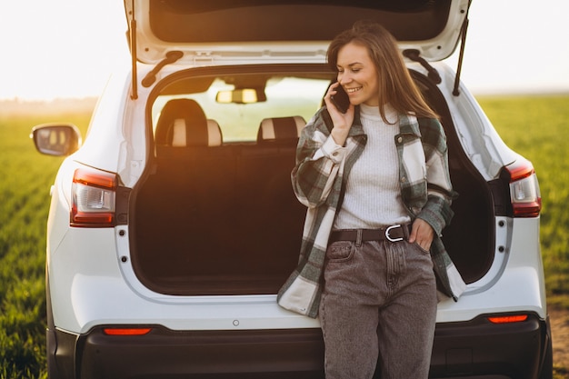 Woman using phone and standing by the car in a field