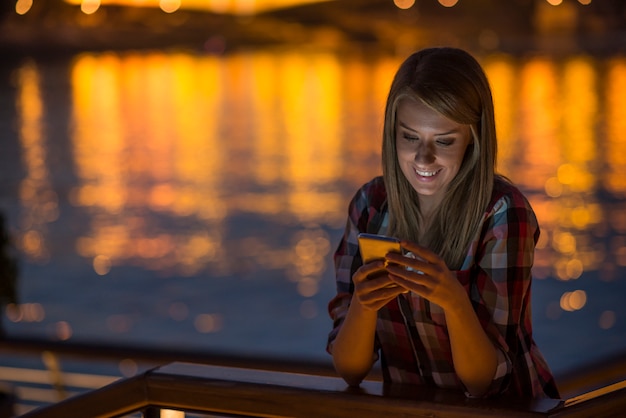 woman using smartphone in city at night. Woman sending text message on phone