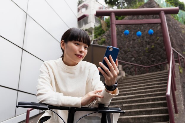 市内でスマートフォンと電動自転車を使用している女性