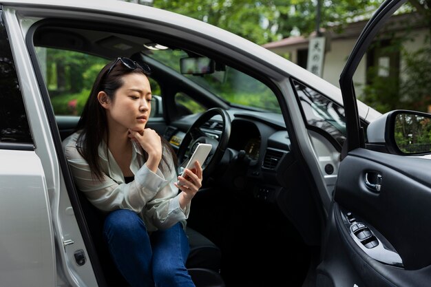 電気自動車でスマートフォンを使用している女性