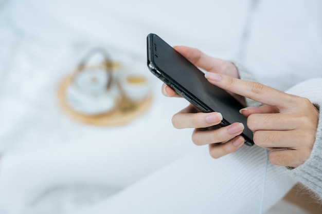 Woman using smartphone on her bed in cold day