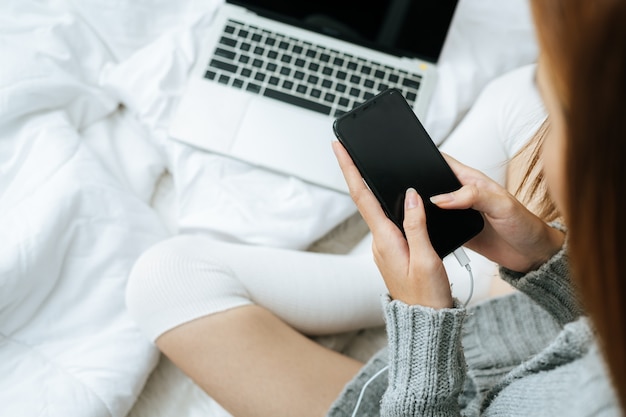 Woman using smartphone on her bed in cold day