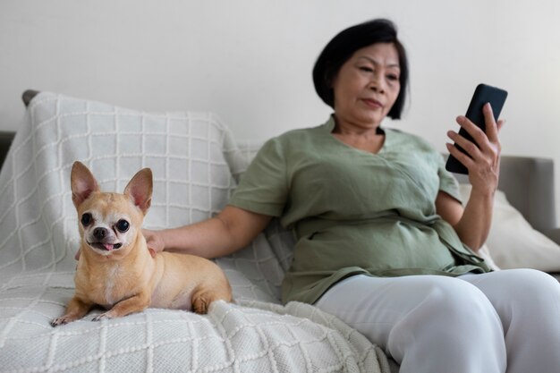 犬の隣で自宅でスマートフォンを使用している女性