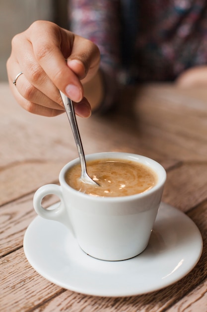 Woman using a spoon to stir the coffee in white cup over table