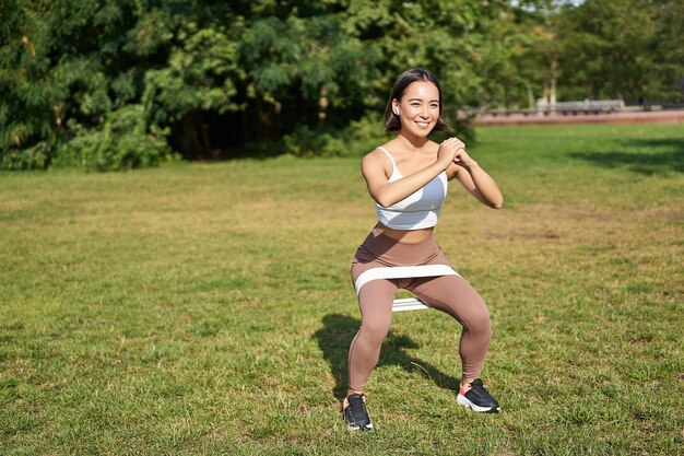 Free photo woman using stretching band resistance fitness rope for workout in park doing squats training on fre