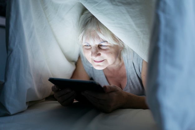 Woman using tablet under blanket