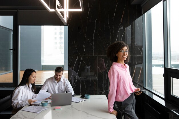 Woman using a tablet to work while her colleagues are using a laptop and documents