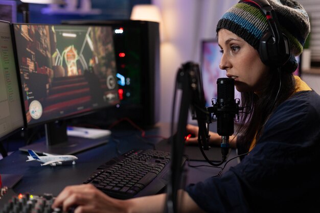 Woman using video games play to stream online on computer. Streamer broadcasting gameplay live with chat on monitor, using headphones and microphone. Player streaming and gaming.