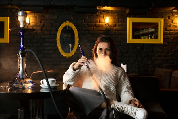 Free photo woman vaping from a hookah in a bar