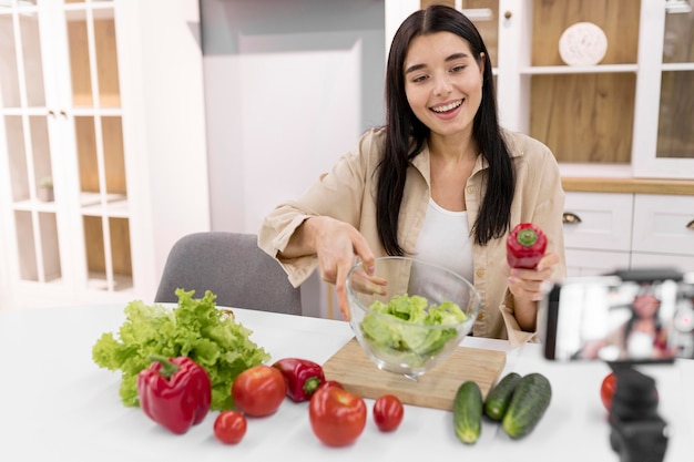 野菜とスマートフォンで家でビデオブログをする女性