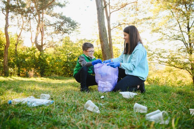 여성 자원 봉사자와 어린 소년이 플라스틱 쓰레기를 주워 야외에서 생분해성 쓰레기 봉투에 넣습니다. 생태, 재활용 및 자연 개념의 보호. 환경 보호.