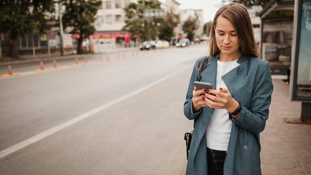 Foto gratuita donna che aspetta l'autobus e cerca il suo telefono cellulare