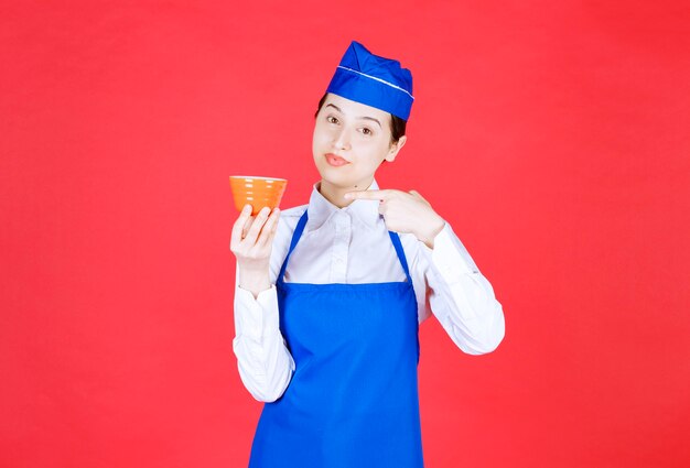 Woman waitress in uniform pointing at an orange bowl on red wall .