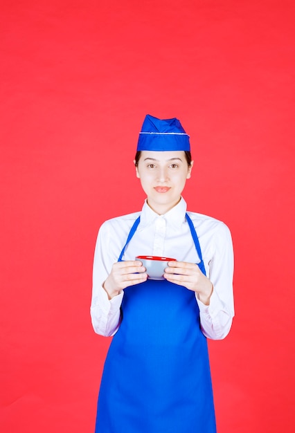 Woman waitress in uniform standing and holding a bowl on red wall.