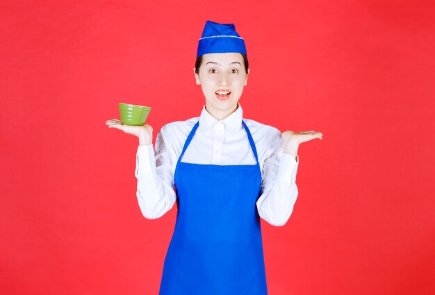 Официантка женщины в униформе стоя и держа зеленую миску.