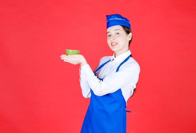 Woman waitress in uniform standing and holding a green bowl .