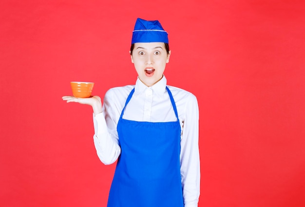 Woman waitress in uniform standing and holding an orange bowl .