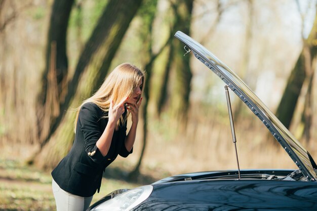 A woman waits for assistance near her car broken down on the road side.