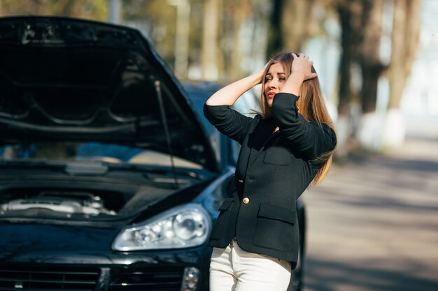 A woman waits for assistance near her car broken down on the road side.