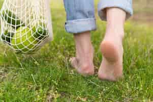 Free photo woman walking barefoot in grass with reusable bag