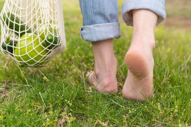 Woman walking barefoot in grass with reusable bag