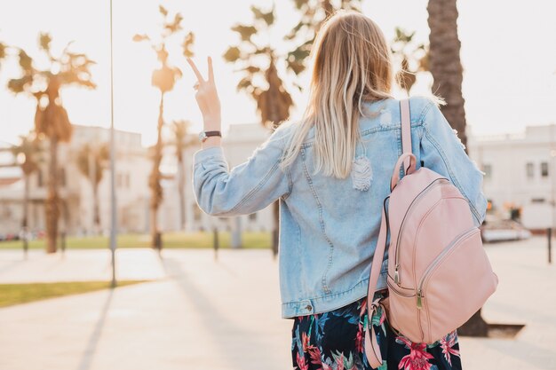 woman walking in city street in stylish denim oversize jacket, holding pink leather backpack