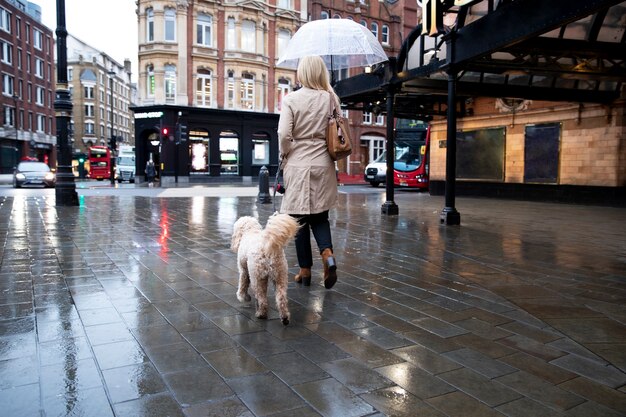 Женщина выгуливает собаку по улицам города во время дождя
