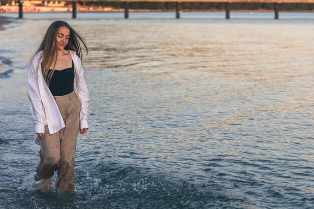 A woman walks along the sea barefoot at sunset copy space