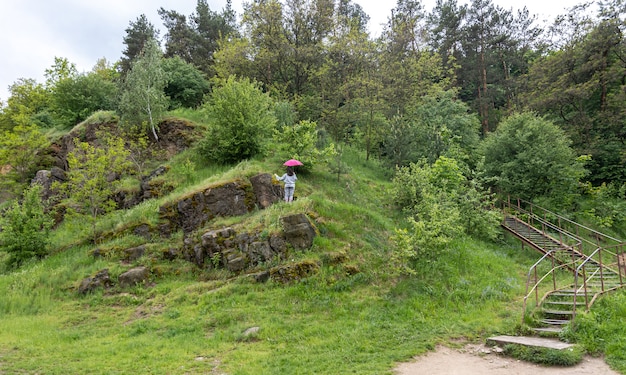 A woman walks under an umbrella in the mountains, among the rocks covered with greenery