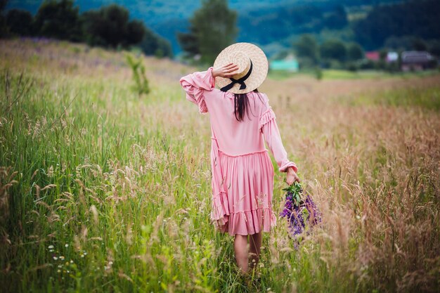 Woman walks with bouquet of lavander across green field 